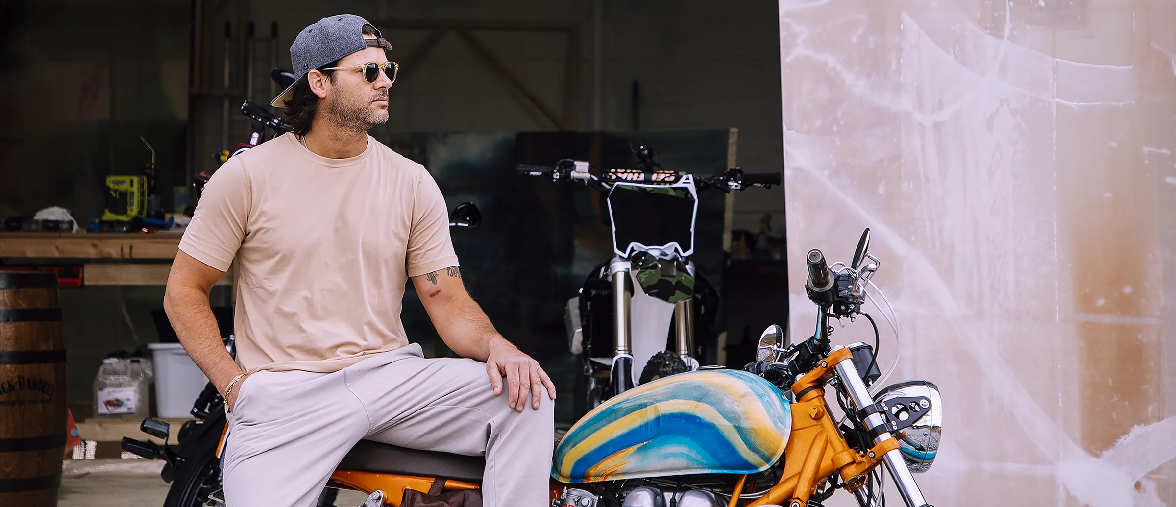 Erik Skoldberg sitting on a custom motorcycle in his workshop, its tank hand-painted in the same marbled blue and white as his canvases